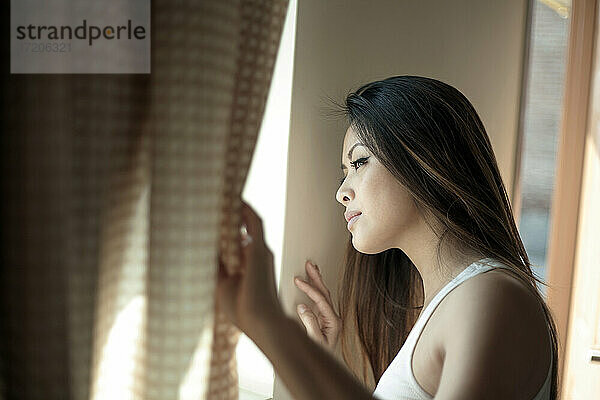 Junge Frau schaut durch ein Fenster im Schlafzimmer
