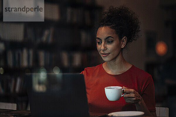 Junge Frau trinkt Kaffee und arbeitet am Laptop im Café