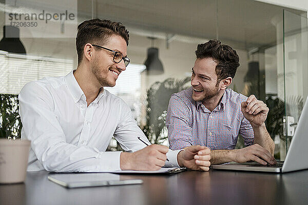 Glückliche männliche Unternehmer mit Laptop auf dem Schreibtisch im Büro