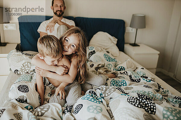 Vater beobachtet Mädchen und Jungen beim Spielen im Bett