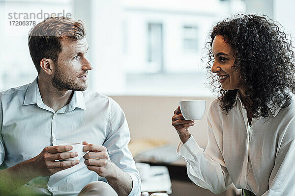 Lächelnde Geschäftsfrau  die mit einem Kollegen Kaffee trinkt  während sie im Cafe sitzt