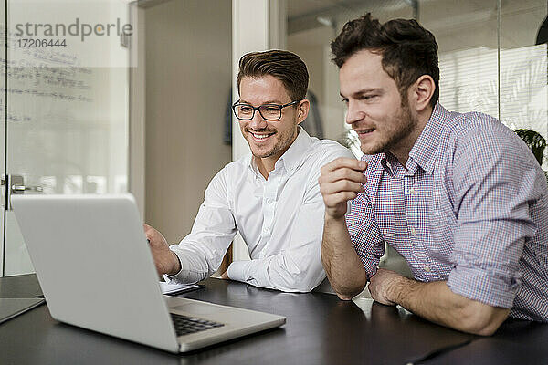 Männlicher Unternehmer arbeitet am Laptop mit einem Kollegen im Büro