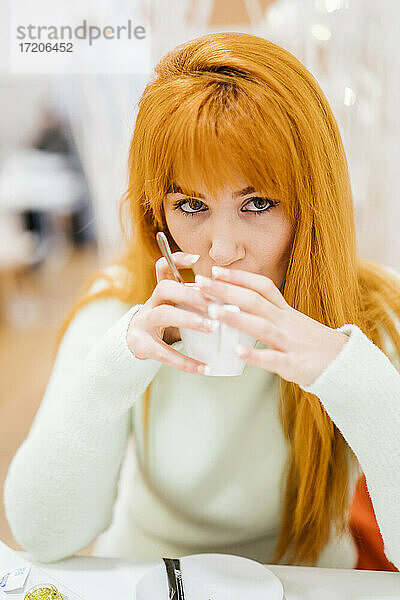 Rothaarige Frau trinkt in einem Café Kaffee und schaut dabei weg