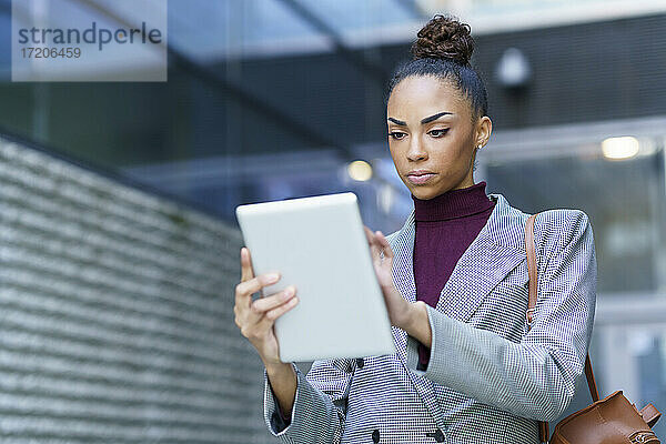 Unternehmer mit Tasche  der ein digitales Tablet benutzt  während er an der Außenseite eines Bürogebäudes steht