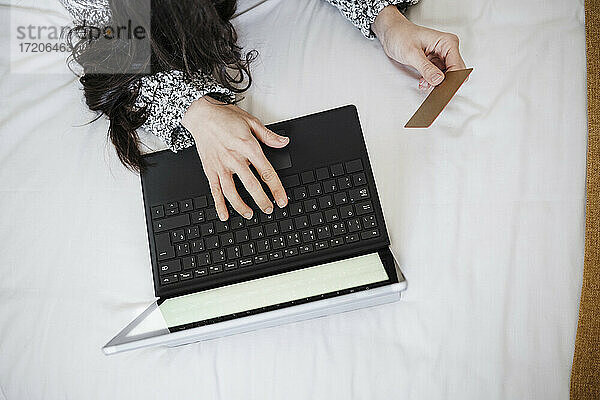 Frau mit Kreditkarte beim Online-Shopping mit Laptop auf dem Bett