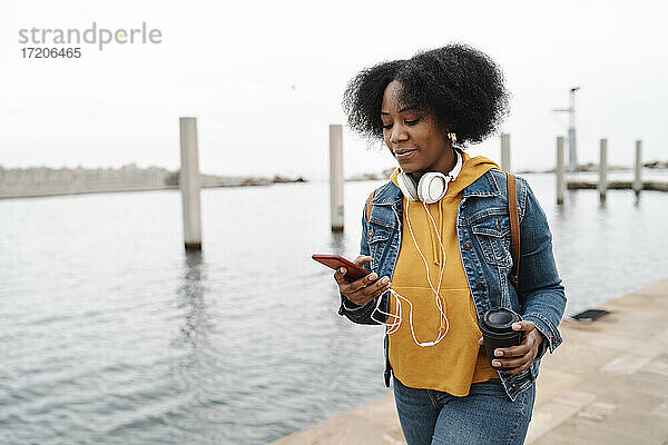 Junge Frau benutzt ihr Smartphone bei einem Spaziergang am Wasser