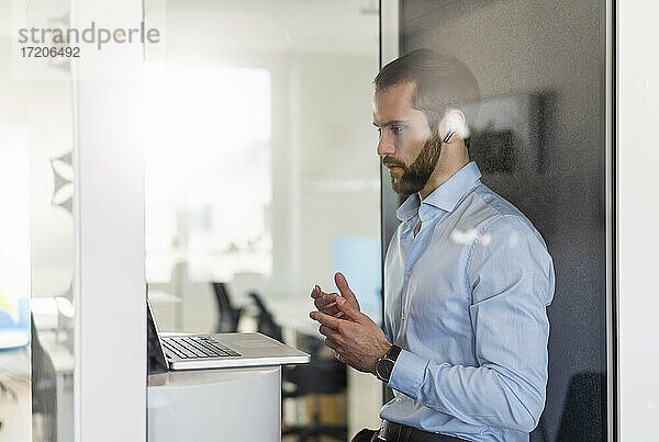 Männlicher Berufstätiger  der einen Videogespräch über einen Laptop in einer Telefonzelle im Büro führt