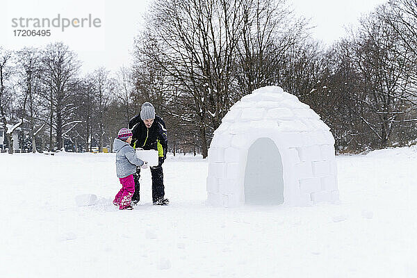Vater hilft seiner Tochter beim Tragen eines Schneeblocks im Park