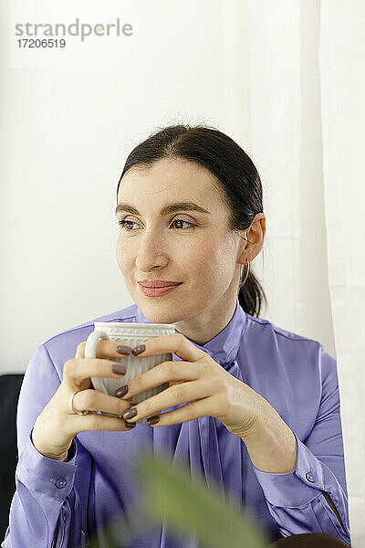 Nachdenkliche Geschäftsfrau hält Kaffeebecher zu Hause