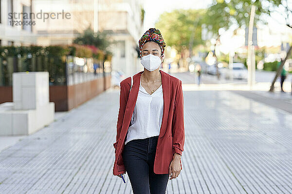 Junge Frau mit Kopftuch und Gesichtsschutzmaske auf dem Gehweg