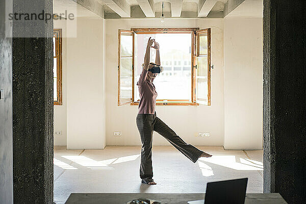 Frau tanzt  während sie zu Hause ein Video im Virtual-Reality-Simulator betrachtet