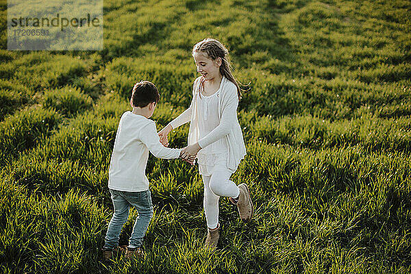 Junge und Mädchen halten sich an den Händen  während sie an einem sonnigen Tag im Gras spielen