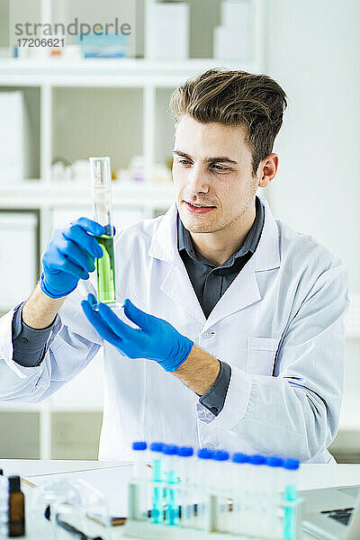 Gut aussehender männlicher Wissenschaftler  der bei der Arbeit im Labor eine Flüssigkeit in einem Zylinder untersucht