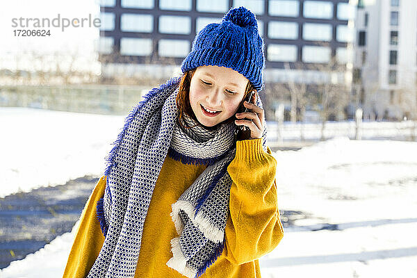 Mädchen in warmer Kleidung  das mit einem Mobiltelefon vor einem Gebäude spricht