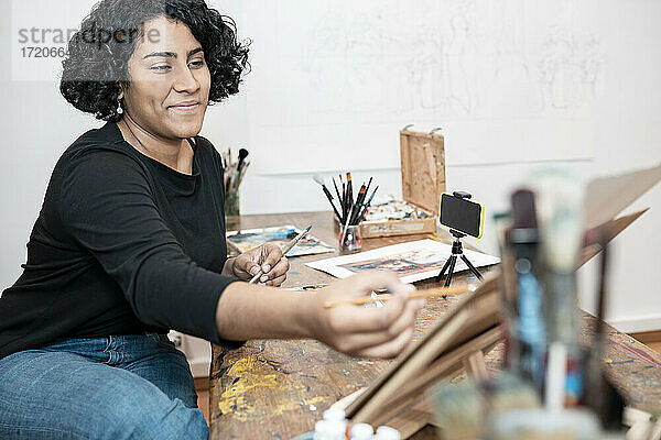 Lächelnde Malerin  die in einem Kunstatelier mit ihrem Mobiltelefon telefoniert