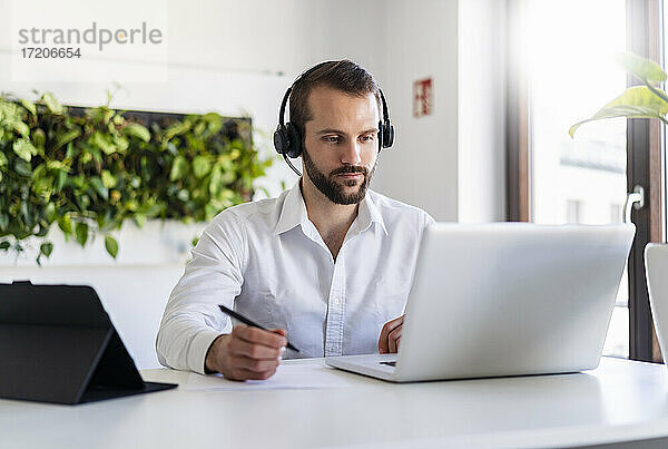 Unternehmer mit Kopfhörern bei der Arbeit am Laptop im Büro