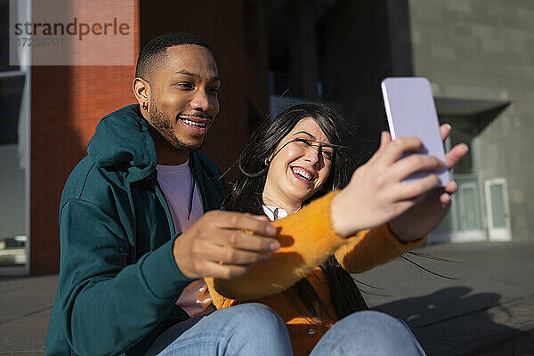 Fröhliche Frau mit Freund nimmt Selfie durch Handy