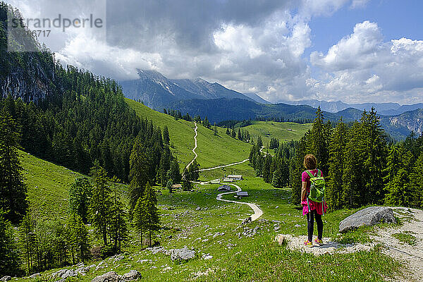 Wanderin steht mitten auf einem Wanderweg  der sich durch ein Sommertal in den Berchtesgadener Alpen schlängelt