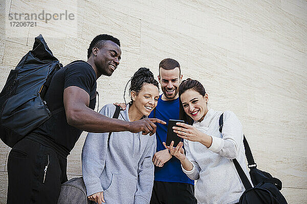 Lächelnde männliche und weibliche Sportler mit Smartphone an der Wand