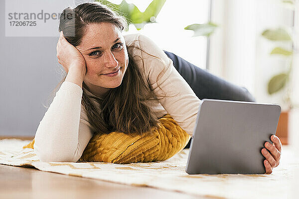 Entspannte Frau mit digitalem Tablet  die zu Hause auf dem Teppich liegt