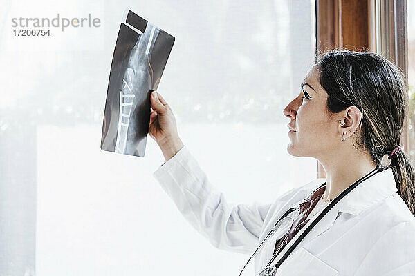 Weibliches medizinisches Fachpersonal  das ein Röntgenbild eines Knochens durch ein Fenster betrachtet