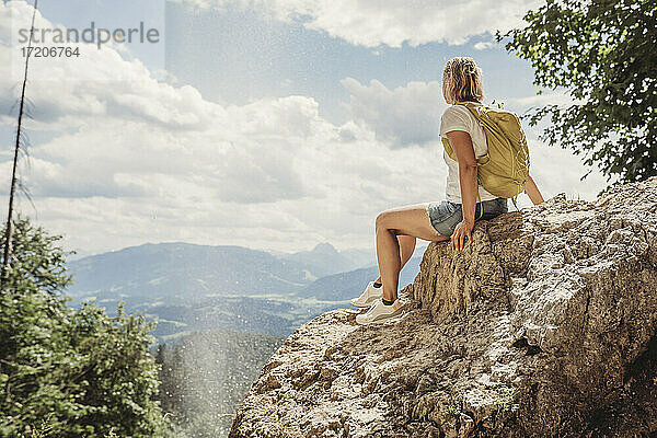 Ältere Frau sitzt auf einem Felsen und betrachtet die Aussicht gegen den bewölkten Himmel