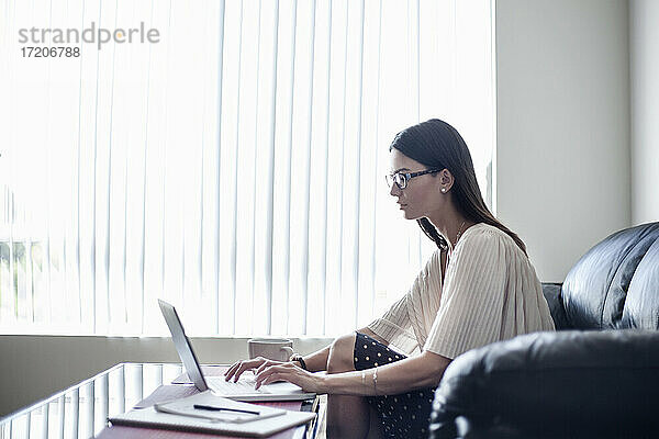 Junge Frau mit Brille  die zu Hause sitzend am Laptop arbeitet