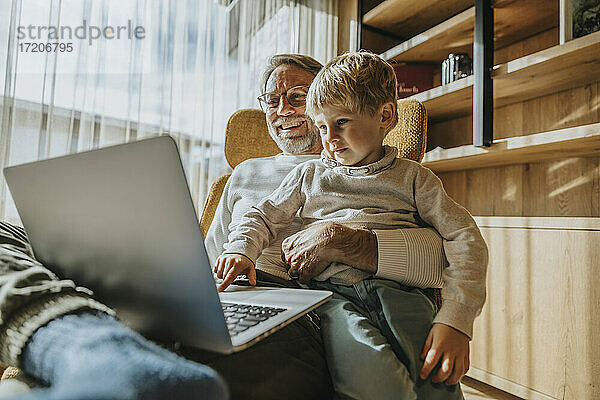 Junge benutzt Laptop  während er mit seinem Vater auf einem Stuhl sitzt