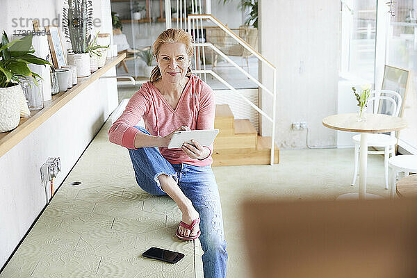 Frau mit digitalem Tablet auf der Arbeitsplatte zu Hause sitzend