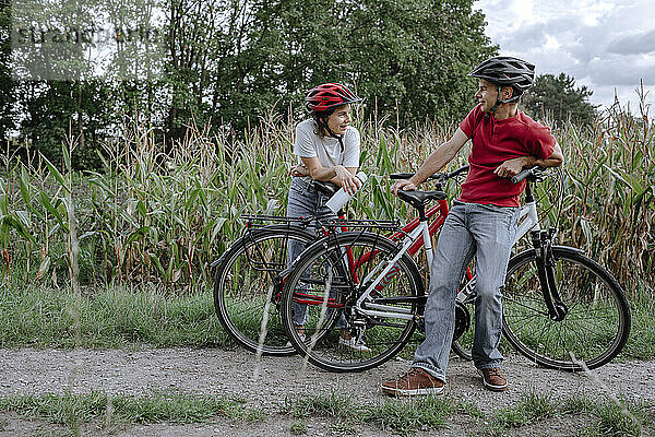 Vater und Tochter unterhalten sich auf einem landwirtschaftlichen Feld  während sie sich auf ein Fahrrad stützen