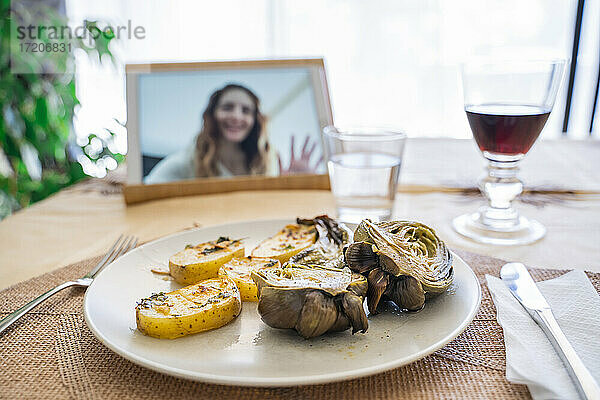 Mittagessen am Tisch  während Frau auf dem Bildschirm eines digitalen Tablets zu sehen ist