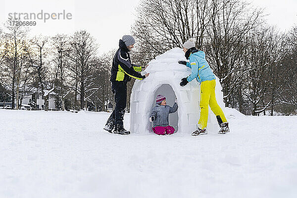 Vater und Mutter helfen ihrer Tochter beim Bau eines Iglus im Schnee im Park
