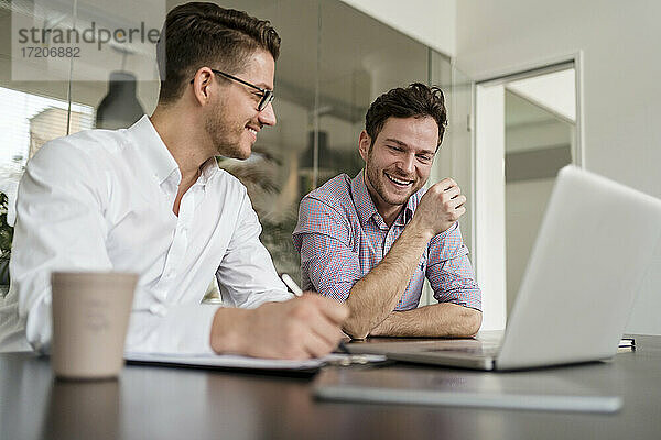 Geschäftsleute  die lächelnd über einen Laptop im Büro diskutieren