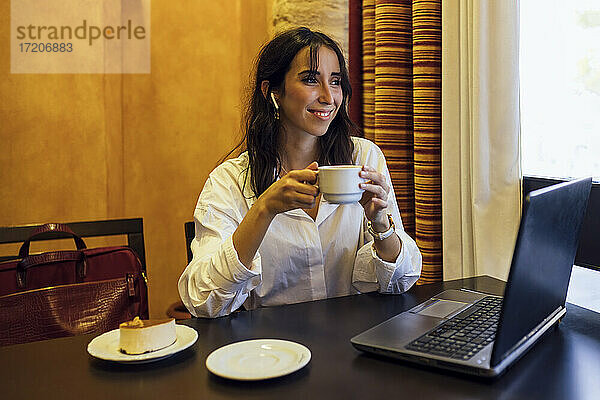 Glückliche junge Geschäftsfrau  die mit einer Tasse Kaffee in der Hand in ein Café schaut