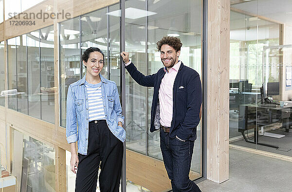 Lächelnde männliche und weibliche Unternehmer stehen vor einer Glaswand im Büro
