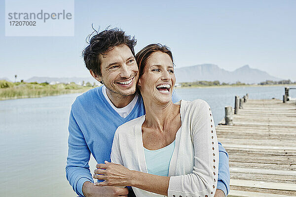 Fröhliche Frau sitzt mit lächelndem Mann auf dem Pier