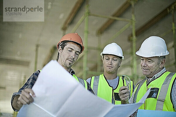 Männliche Bauarbeiter besprechen Pläne auf der Baustelle