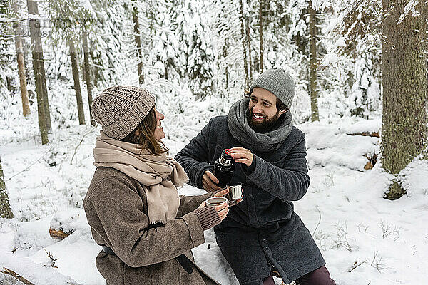 Junges Paar lächelt bei einem Kaffee im Wald im Winter