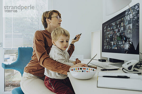 Mutter am Computer  während ihr Sohn im Büro auf dem Schoß sitzt