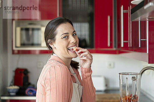 Fröhliche Frau  die in der Küche ein Stück Erdbeere isst