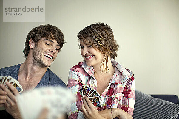 Lächelndes Paar spielt mit einem Freund Karten  während es zu Hause sitzt