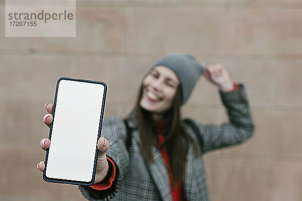 Frau zeigt leeren Smartphone-Bildschirm gegen die Wand