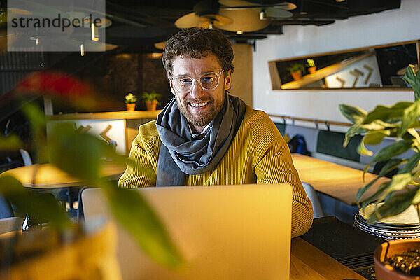 Glücklicher männlicher Besitzer mit Laptop im Cafe sitzend