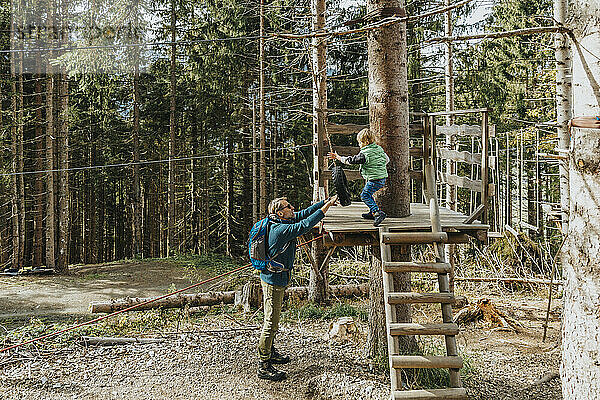 Vater hält Tier  während Sohn im Wald Seilgarten macht