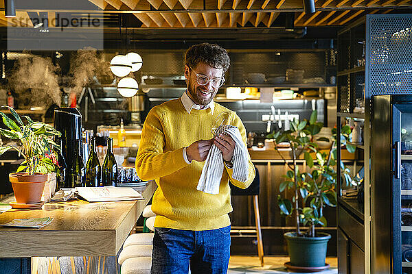Lächelnder männlicher Café-Besitzer beim Reinigen von Weingläsern im Café