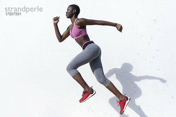 Weibliche Läuferin springt beim Üben gegen eine weiße Wand