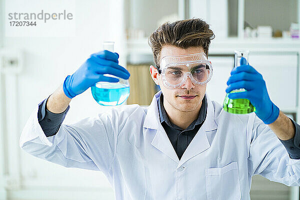 Männlicher Wissenschaftler hält chemische Flaschen im Labor