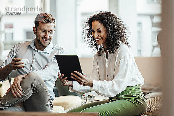 Lächelnde Geschäftsfrau  die ein digitales Tablet benutzt  während sie mit einem Kollegen in einem Cafe sitzt