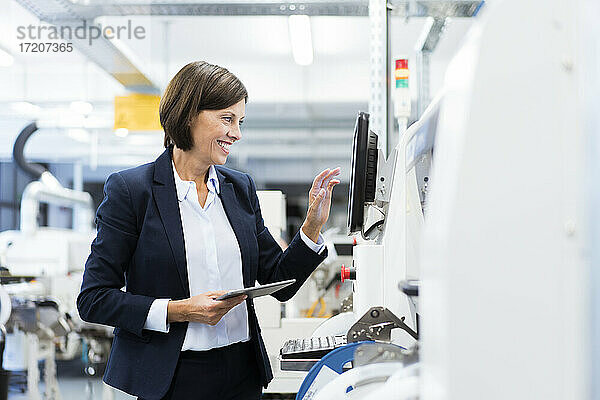 Glückliche Geschäftsfrau mit digitalem Tablet  die Maschinen in einer Fabrik bedient