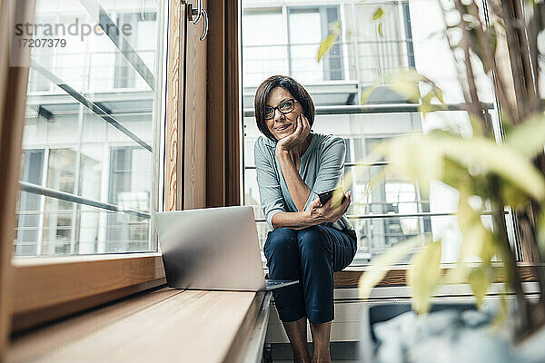 Unternehmerin mit Smartphone  die wegschaut  während sie im Büro sitzt